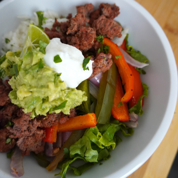 Estos bowls de taco con carne molida están acompañados con arroz con limón y culantro, frijoles negros, carne molida sazonado, pimientos y cebollas asadas, lechuga picada, pimientos, yogur griego y  guacamole. ¡Estos bowls son altamente personalizables y es una receta ideal para preparar comidas para una semana de almuerzos!