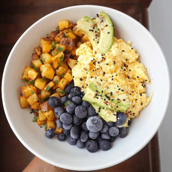 Bowl de desayuno saludable con papas, huevos y palta servido en mesa con luz natural